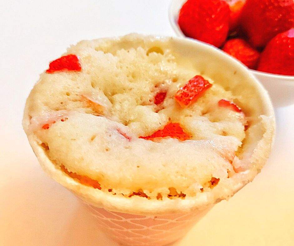 Strawberry mug cake with a bowl of fresh strawberries on the side.