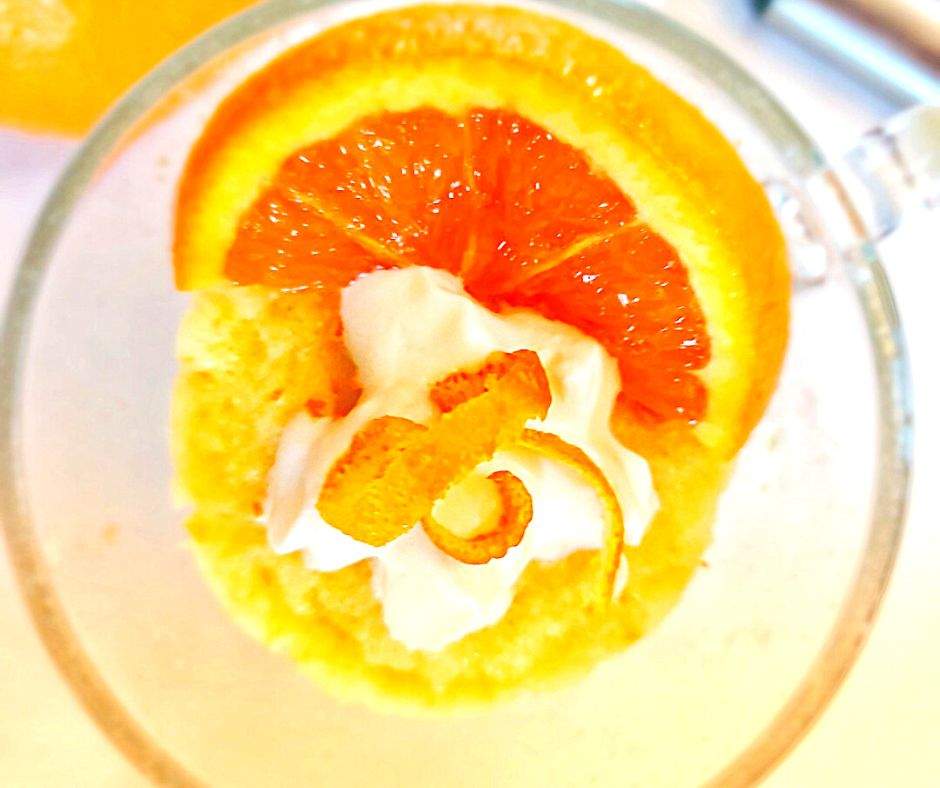 Orange cake in a mug with whipped cream and orange zest